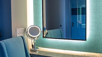 Un bagno con una sedia blu, uno specchio rotondo e un grande specchio a parete.