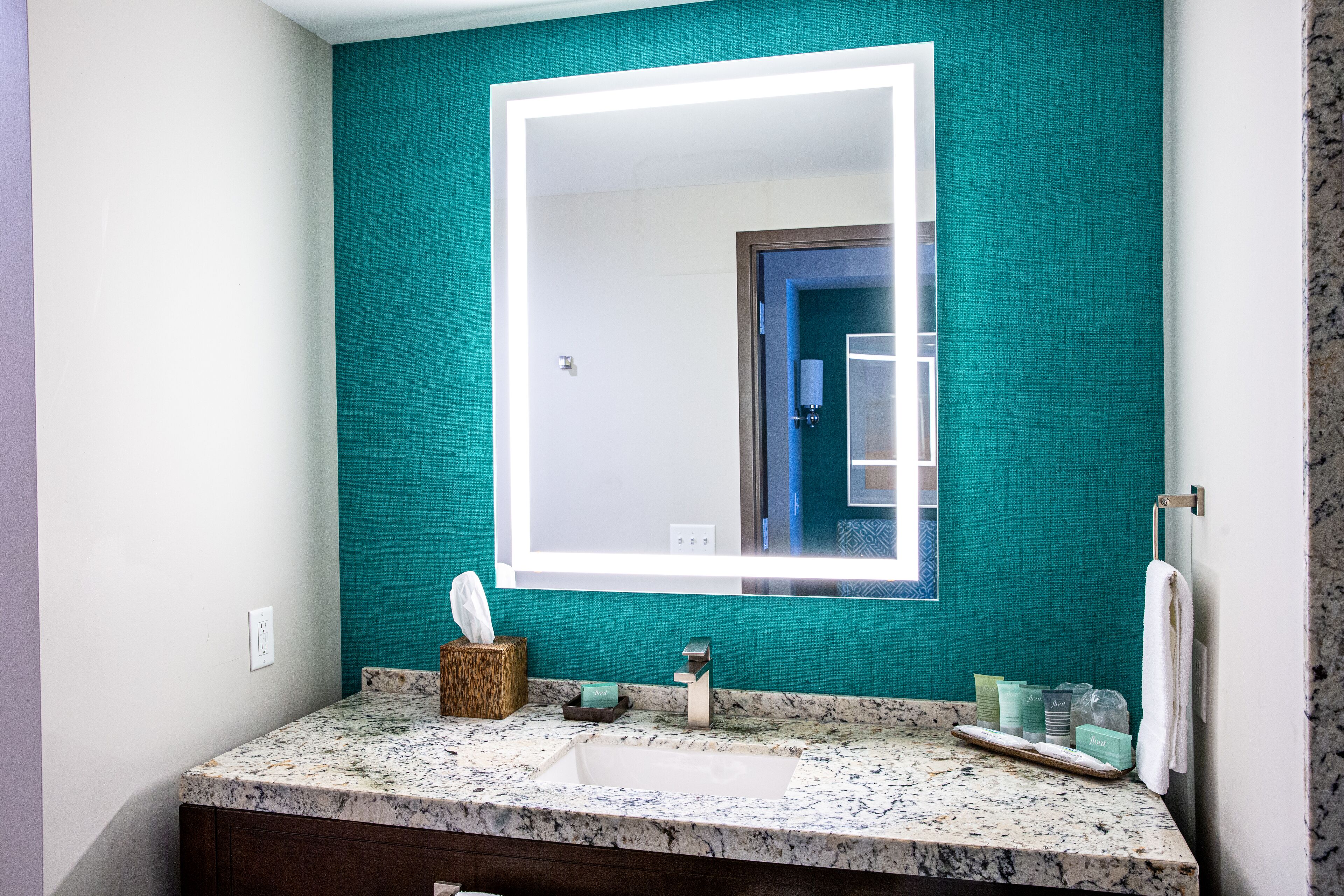 A bathroom with a teal wall, a white sink, and a large mirror.