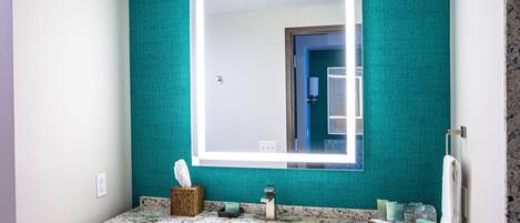 A bathroom with a teal wall, a white sink, and a large mirror.