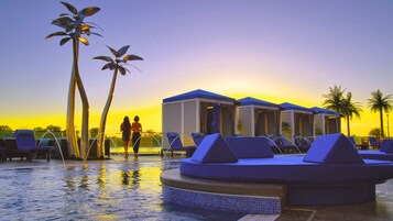 Un área de piscina con sillones reclinables, una piscina pequeña y un edificio con techos azules.