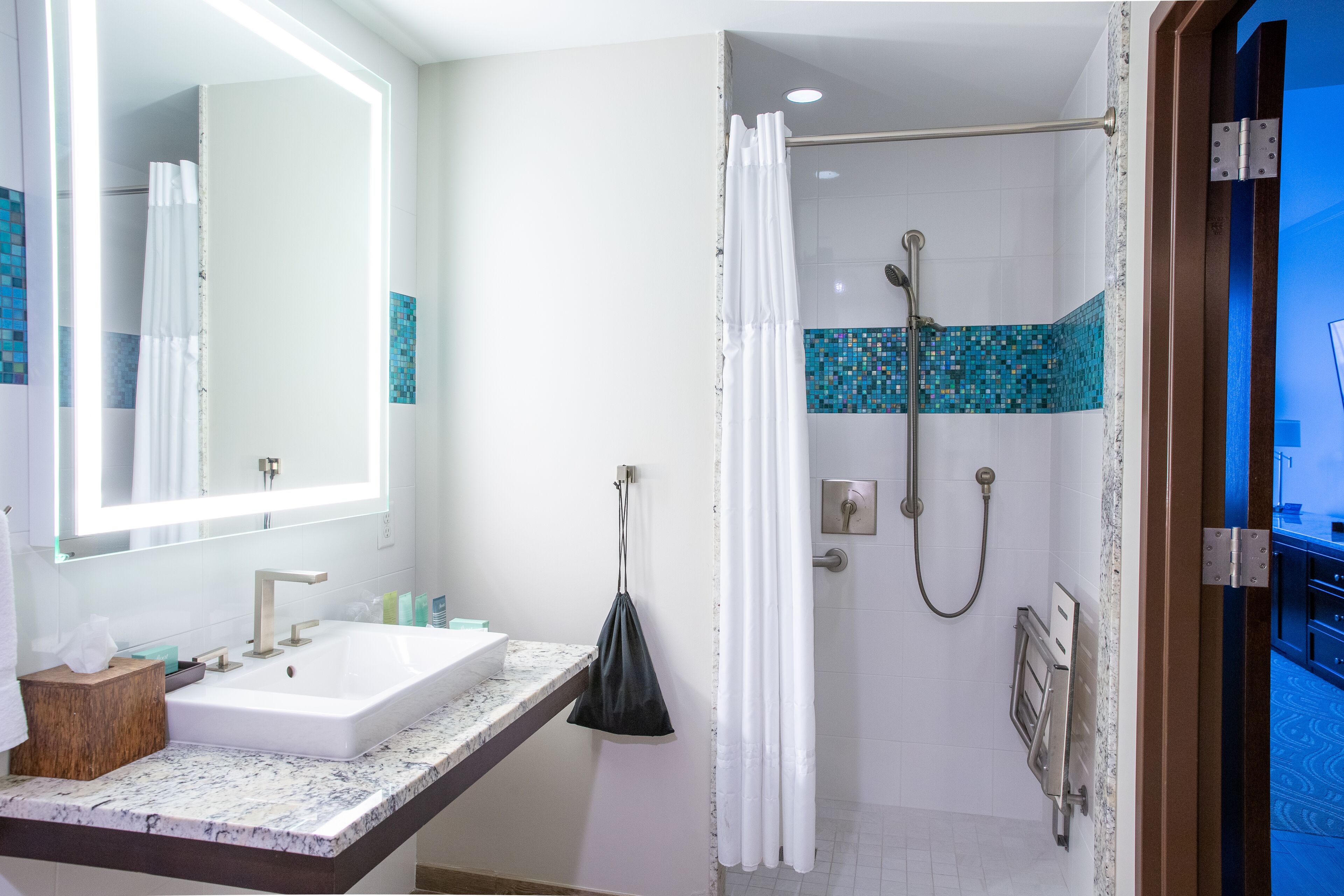 A bathroom with a sink, mirror, shower, and towel rack.