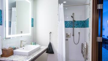 A bathroom with a sink, mirror, shower, and towel rack.
