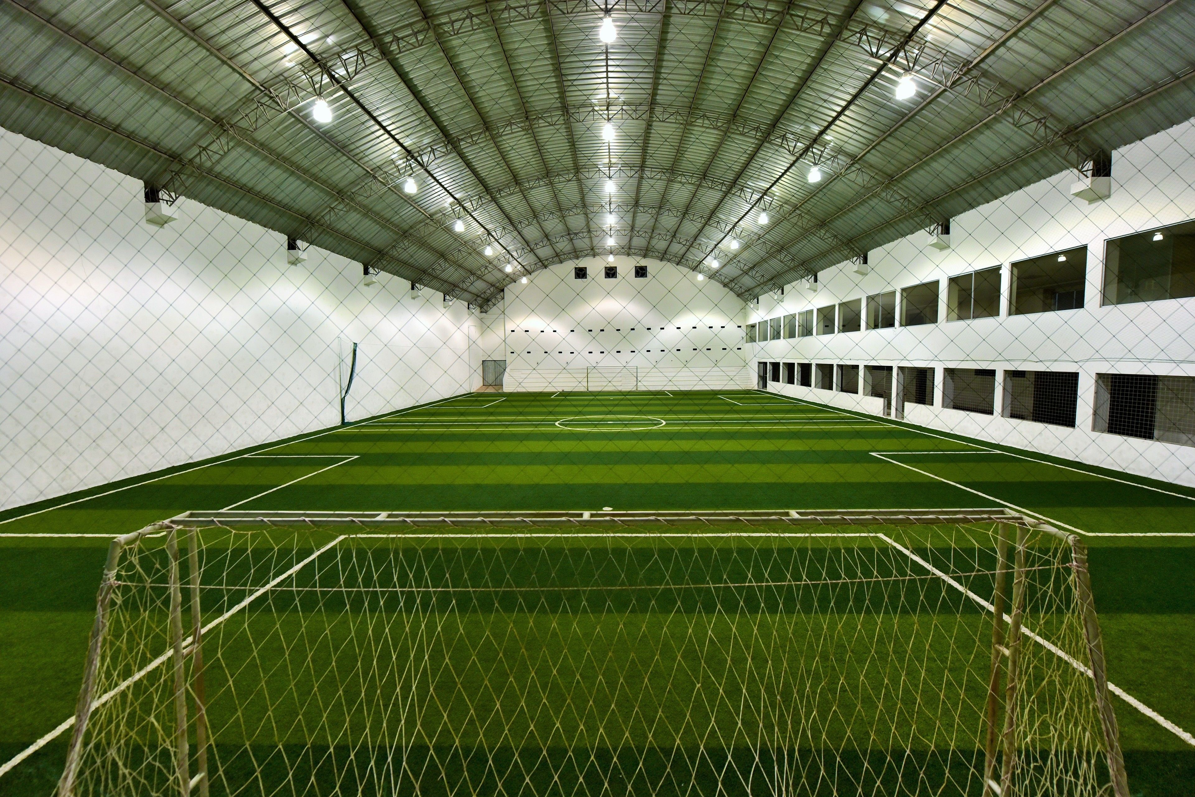 An indoor soccer field with a goal, surrounded by white walls and multiple windows.