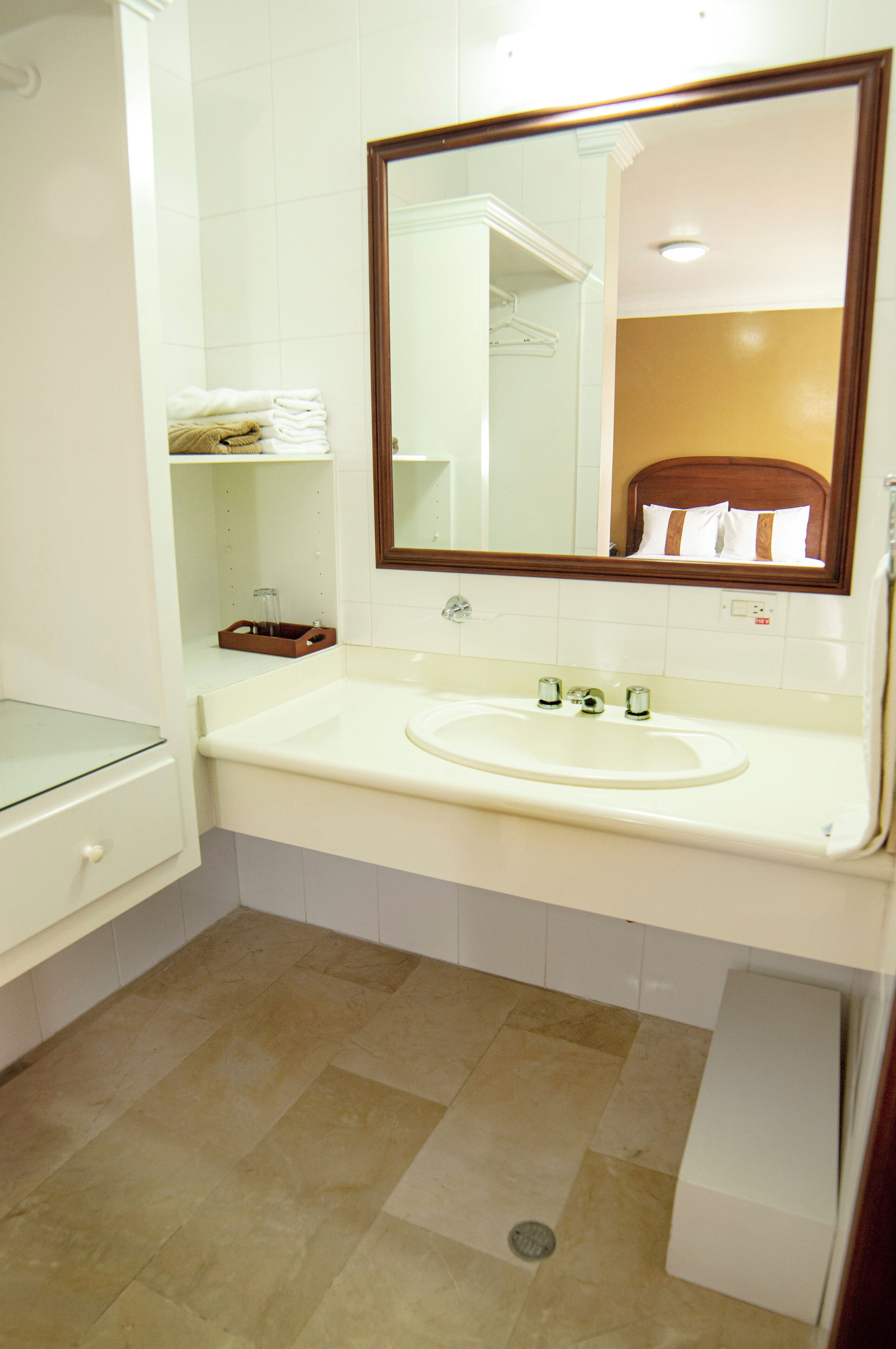 Un baño con un lavamanos blanco, un armario de vidrio y un espejo con marco de madera.