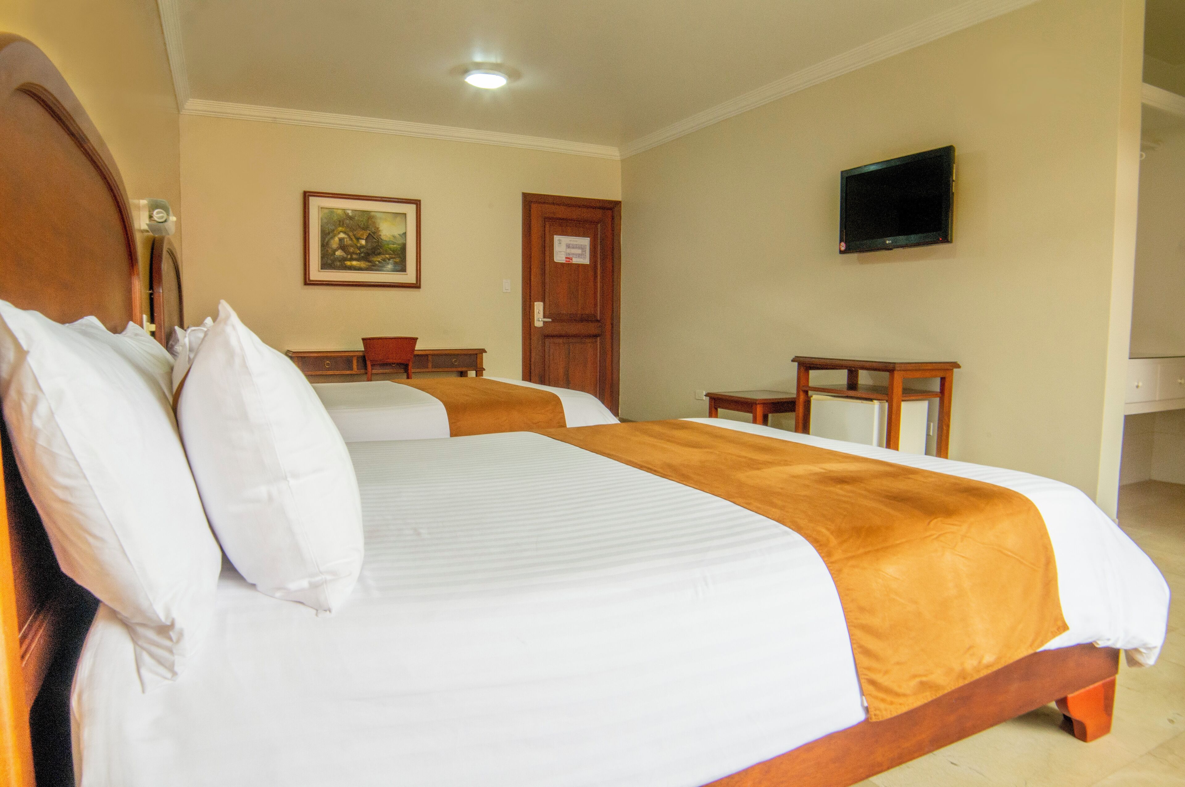 Habitación de hotel con dos camas, cabecera de madera, televisor en la pared y una puerta con un cartel.