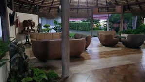 Un vaste espace de détente doté d’un toit de chaume, de sièges confortables et d’un élément décoratif aquatique.