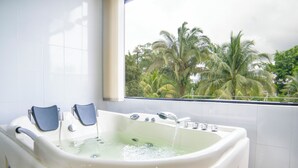Une salle de bain avec une grande baignoire, deux repose-pieds bleus et une fenêtre donnant sur des palmiers.