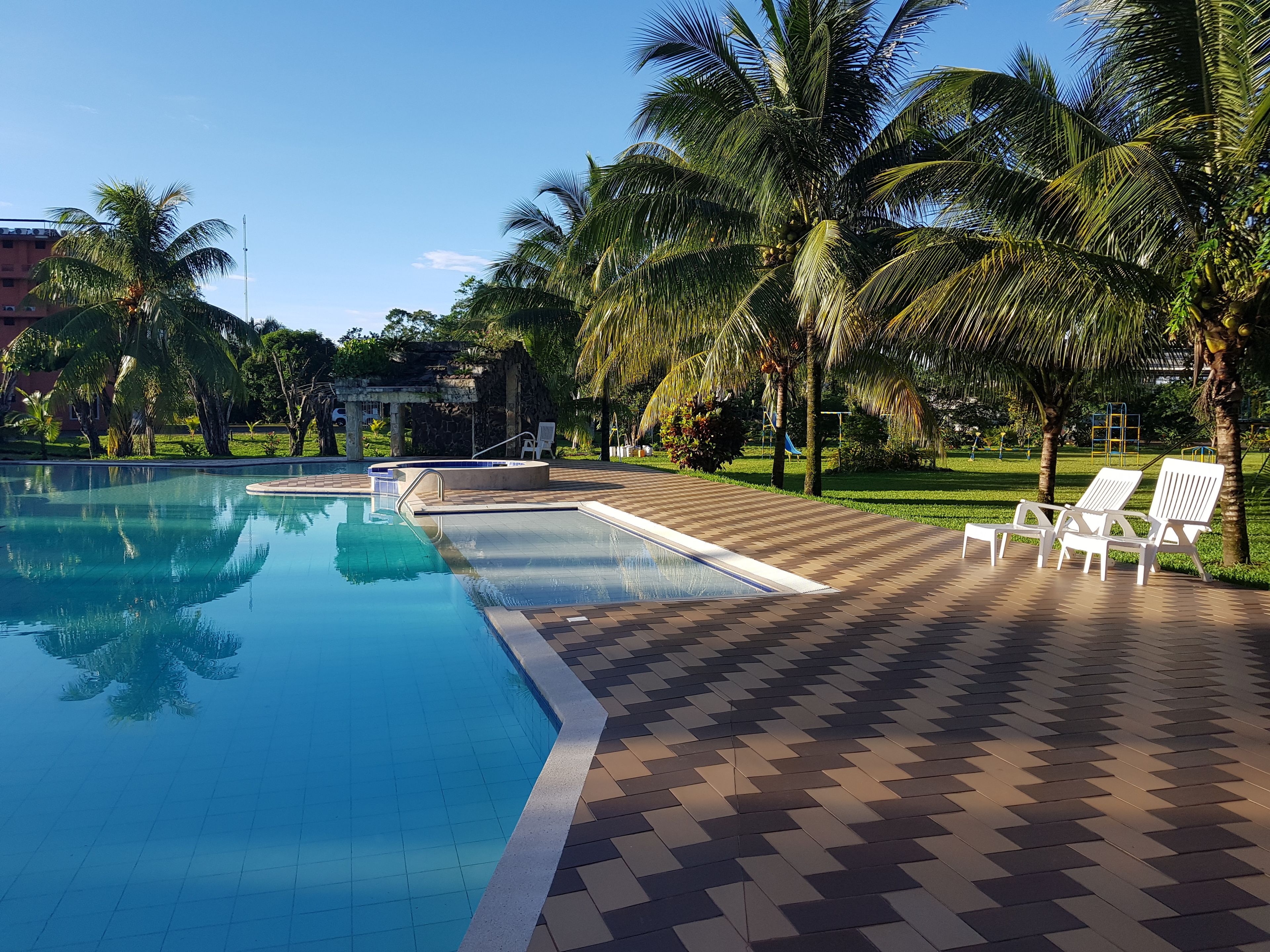 A pool with clear blue water, surrounded by palm trees and a tiled deck with lounge chairs.