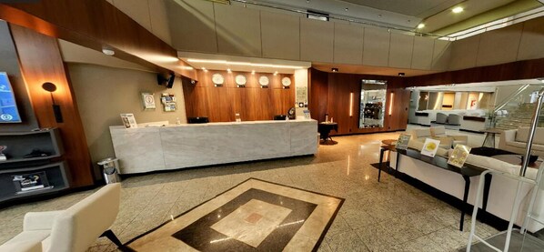 A hotel lobby with a reception desk, seating area, and a staircase. - Premium Vila Velha Ponta Grossa (Ponta Grossa)