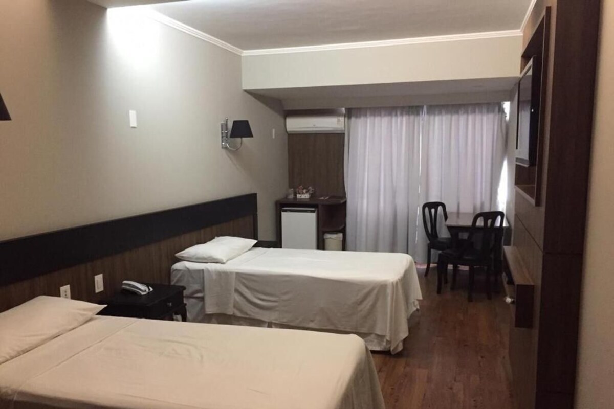 Une chambre d’hôtel avec deux lits, un bureau, une chaise, une télévision et une fenêtre avec des rideaux.