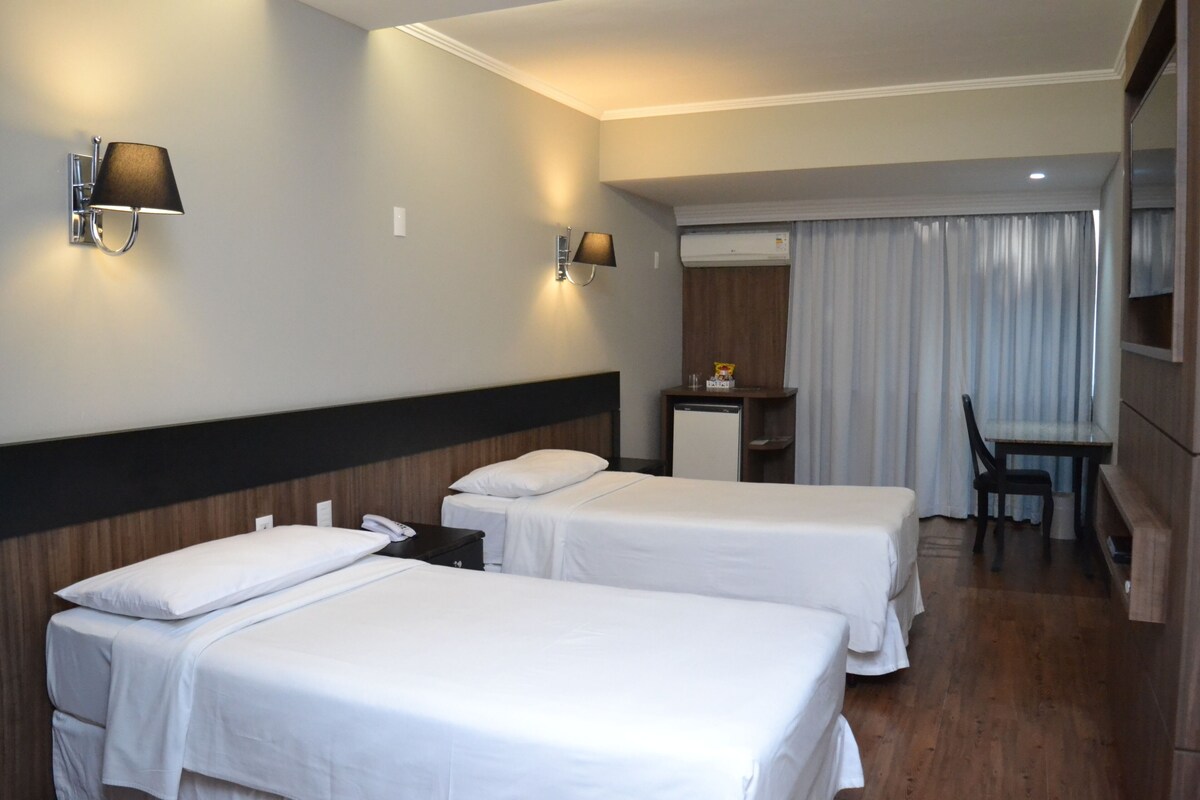 Une chambre d’hôtel avec deux lits simples, un bureau, une chaise et une petite kitchenette.