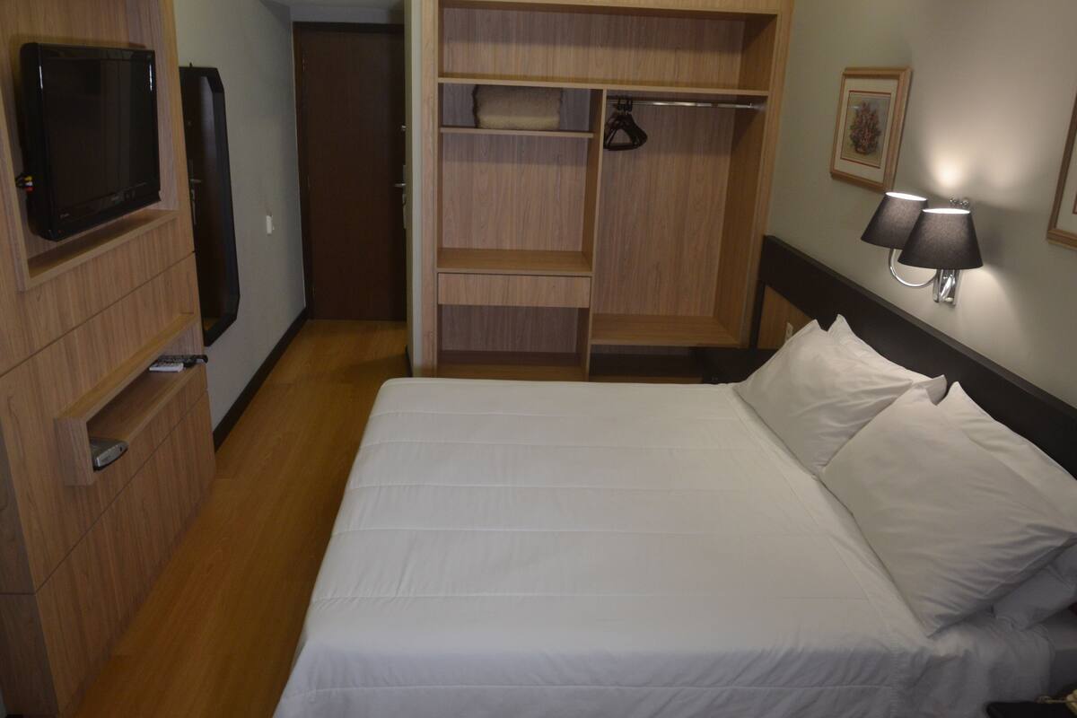 Ein Hotelzimmer mit Bett, Fernseher, Kleiderschrank und Nachttischlampe.