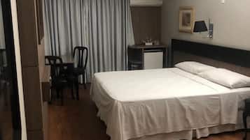 Quarto de hotel com cama, escrivaninha, cadeira, guarda-roupa e janela com cortinas.