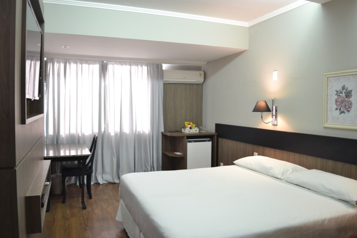 Une chambre d’hôtel comprenant un lit, un bureau, une chaise, un appareil de climatisation, une lampe et un tableau encadré au mur.