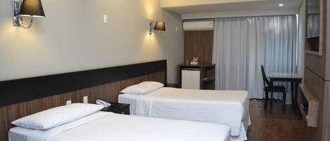 A hotel room with two beds, a desk, a chair, and a minibar.