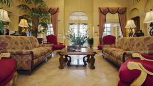 A spacious lobby with two sofas facing a central table, surrounded by potted plants and red chairs. - 3BD 2BA Condo Sleeps 6 Gold RVC30633 Bedroom RHOF (Orlando)