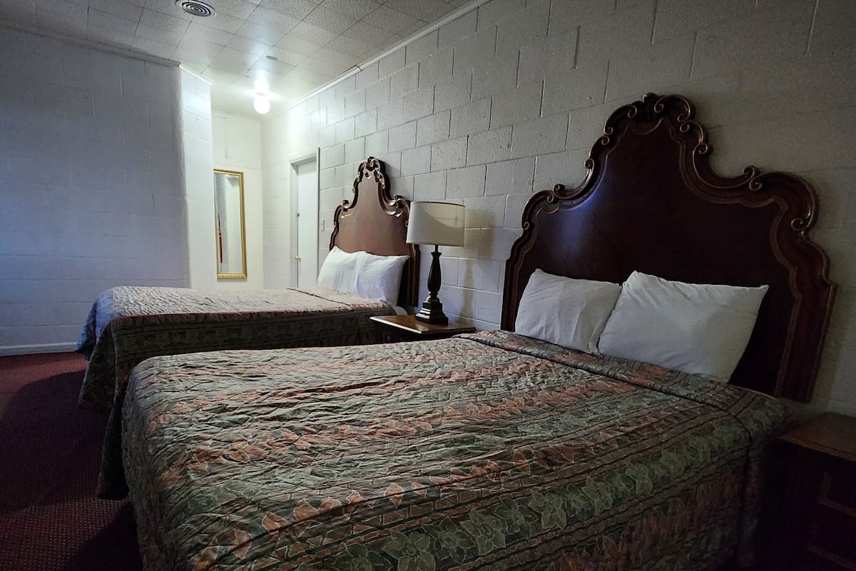 A hotel room with two beds, a mirror, a lamp, and a brick-patterned wall.