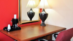 Een hotelkamer met een houten bureau, twee lampen, een koffiezetapparaat en een spiegel.