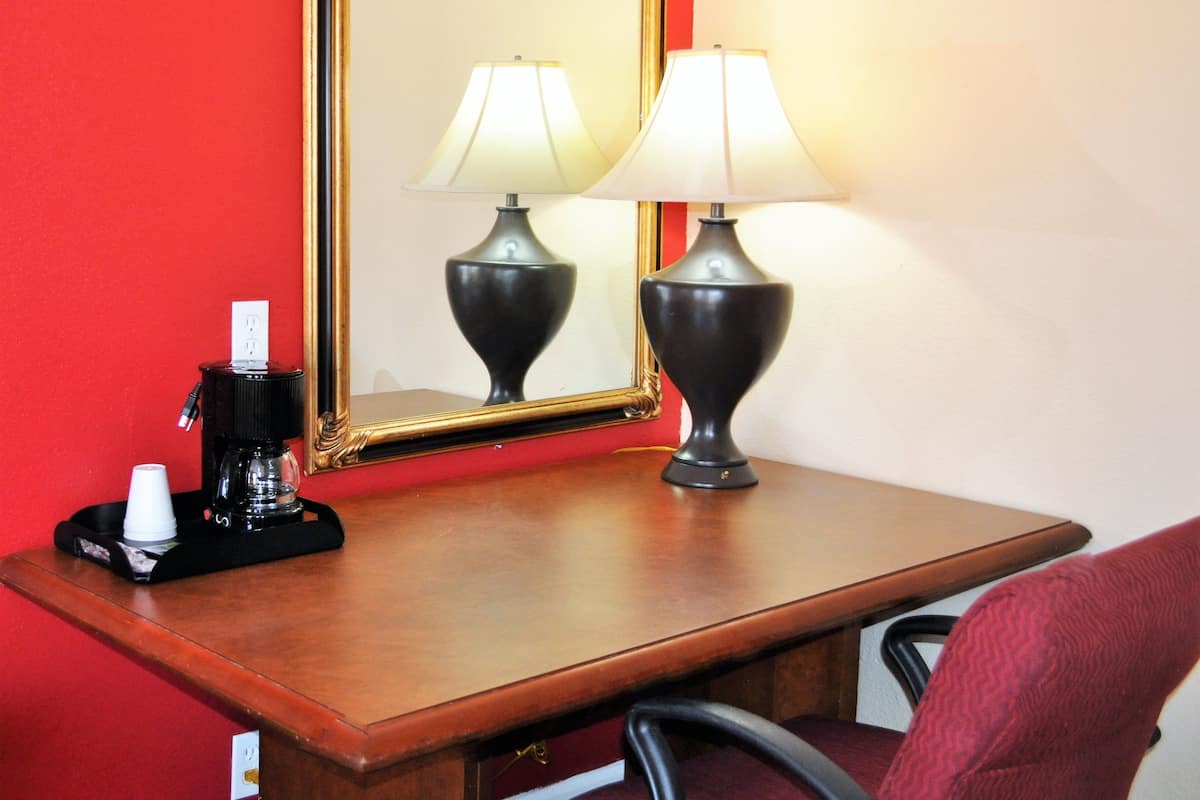 A hotel room with a wooden desk, two lamps, a coffee maker, and a mirror.
