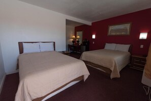 A hotel room with two beds, a desk with a lamp, a chair, and a small table.