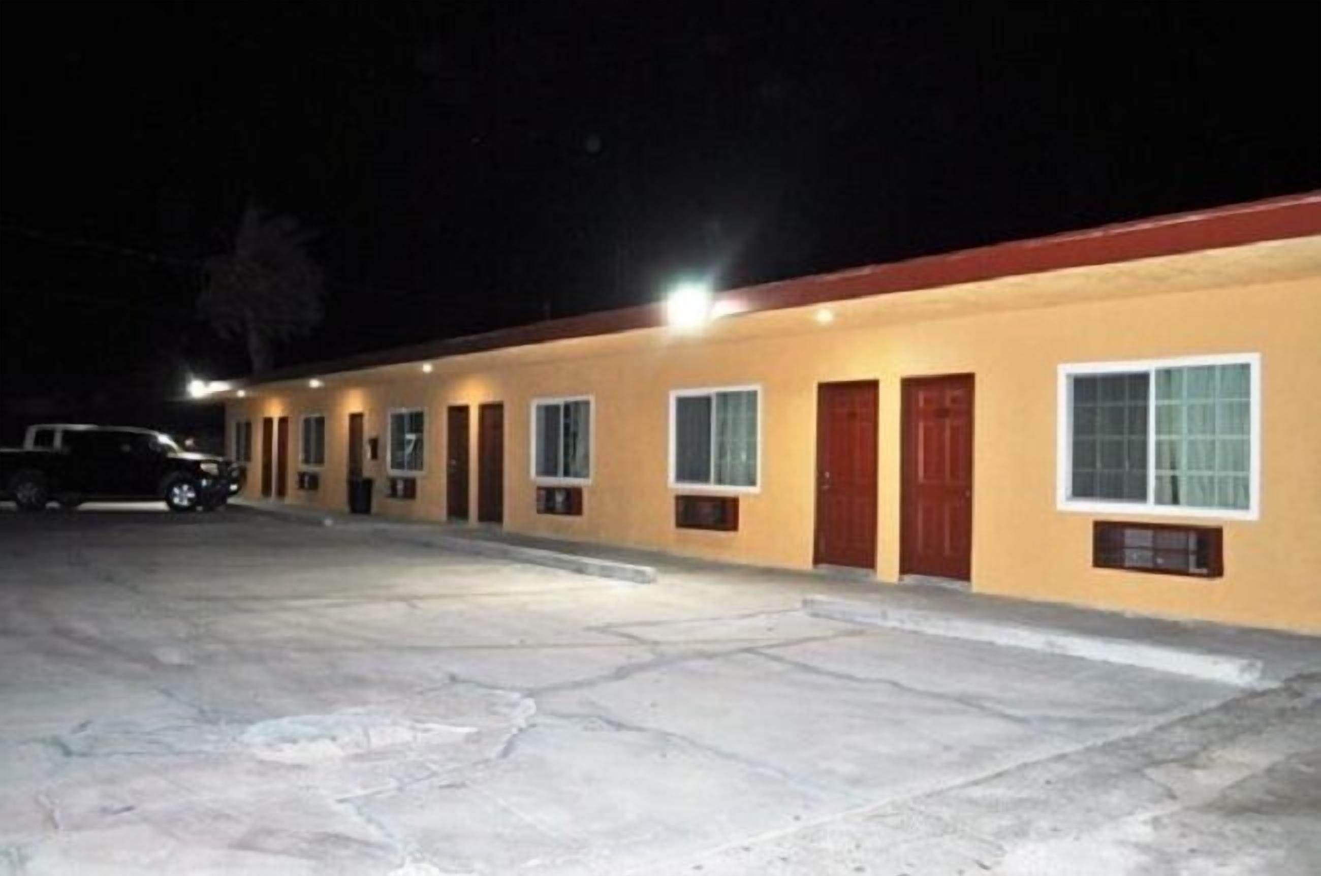 A motel with a row of rooms, each with a door and window, and a parking lot in front.