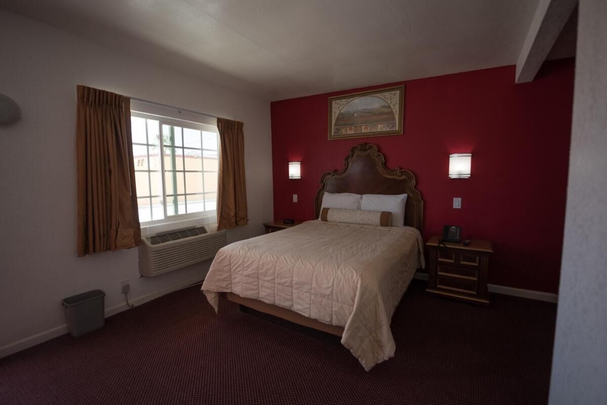 A bedroom with a large bed, a window with curtains, a radiator, and a painting on the wall.