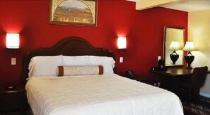 A hotel room with a large bed, two bedside lamps, a desk with a chair, and a painting on the wall.