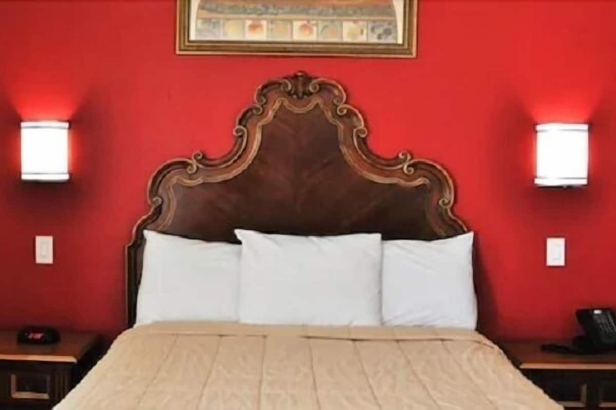 A hotel room with a wooden headboard, two bedside lamps, a bed with white linens, and a nightstand with a telephone.