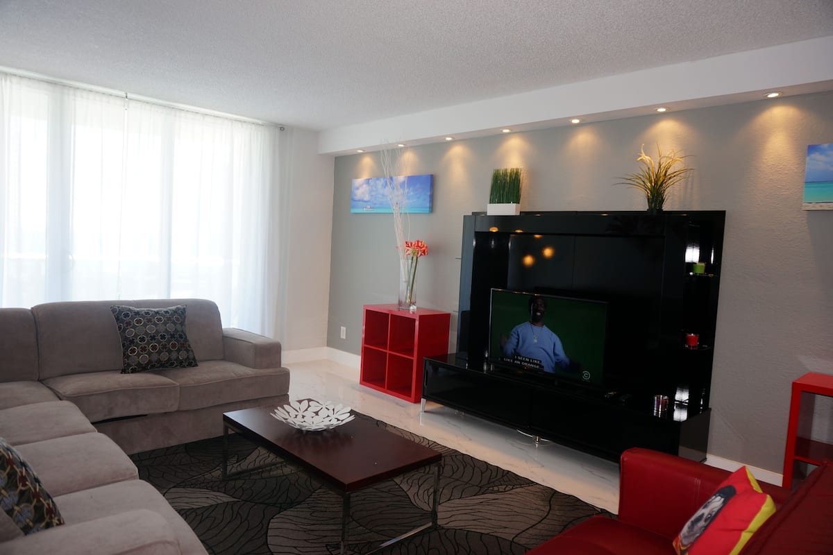 Un salon moderne avec un canapé, un fauteuil rouge, une table basse et un téléviseur à écran plat fixé au mur.