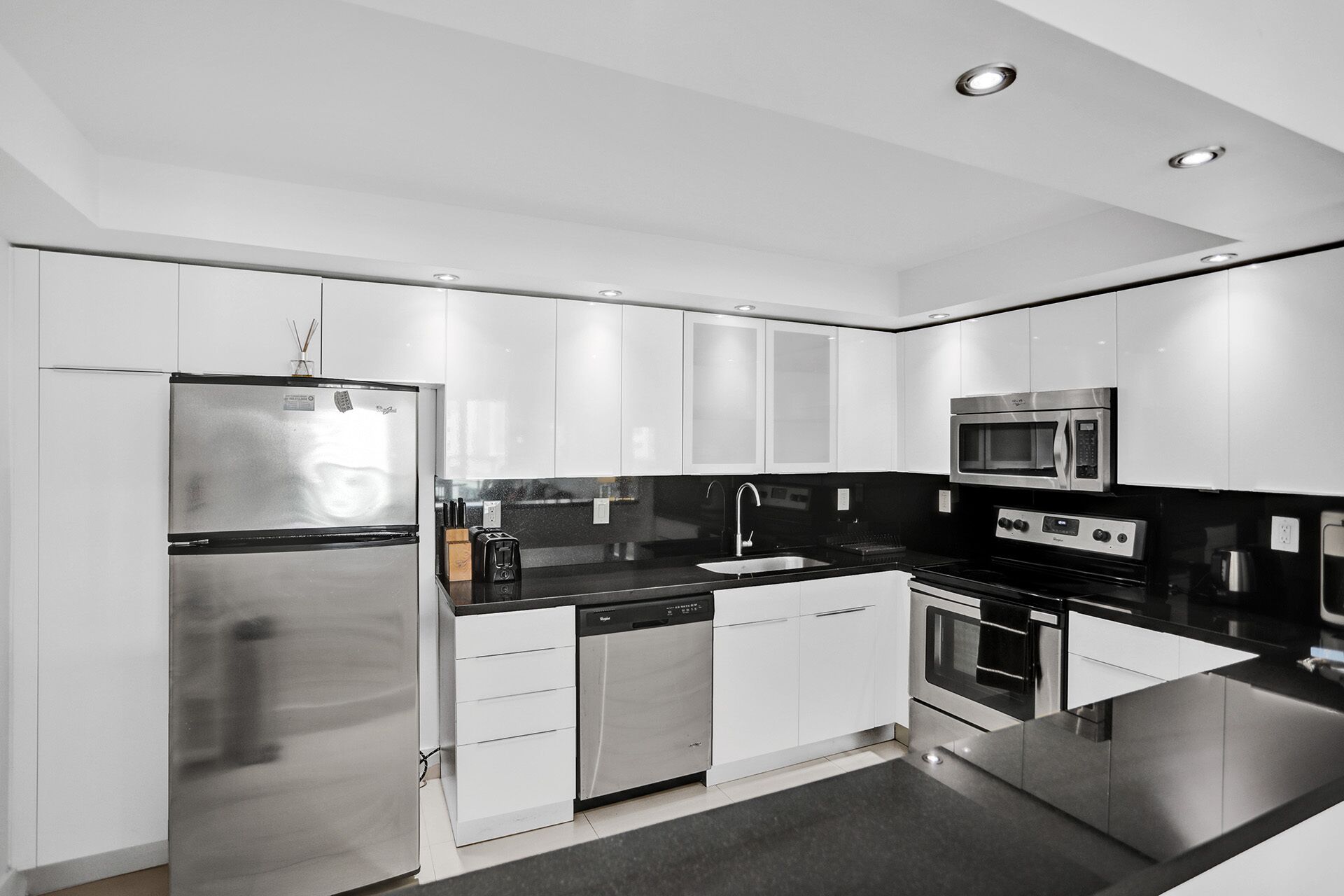 A modern kitchen with stainless steel appliances, white cabinetry, and a black countertop.