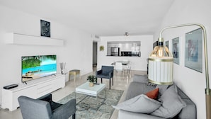 A modern living room with a flat-screen TV, a sofa, a coffee table, and a dining area with chairs. - Ocean Reserve Condominium (Sunny Isles Beach)