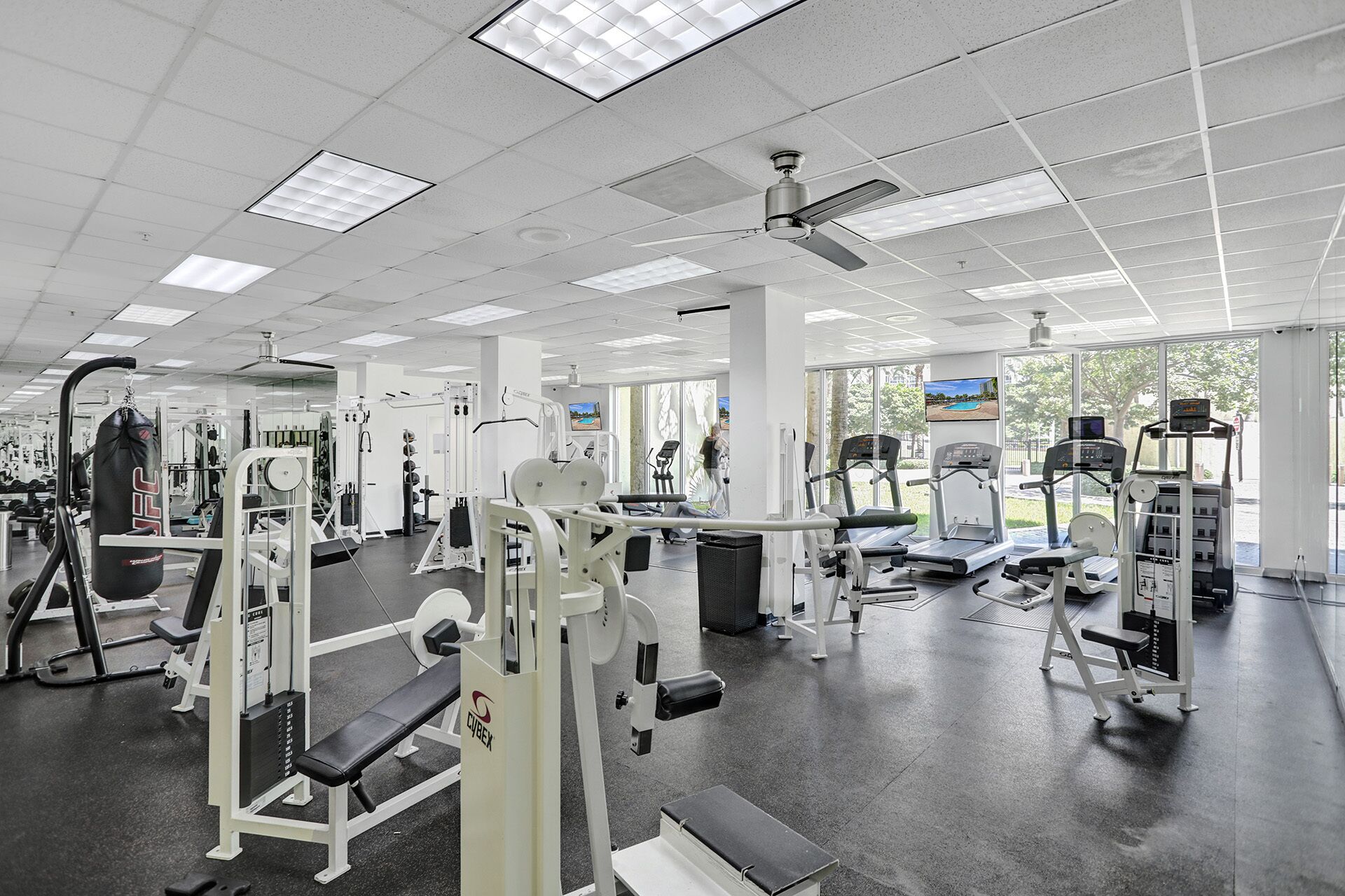 A gym with various exercise equipment, large windows, and a ceiling fan.