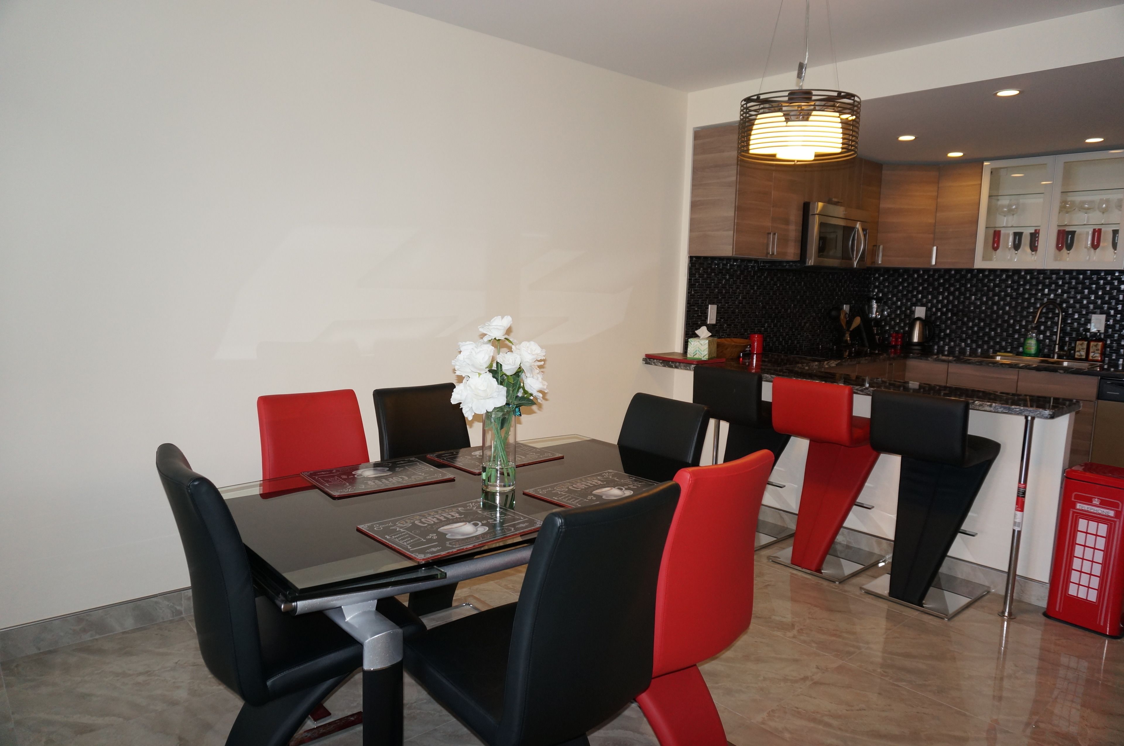 A modern dining area with a black table, red and black chairs, and a vase of white flowers.