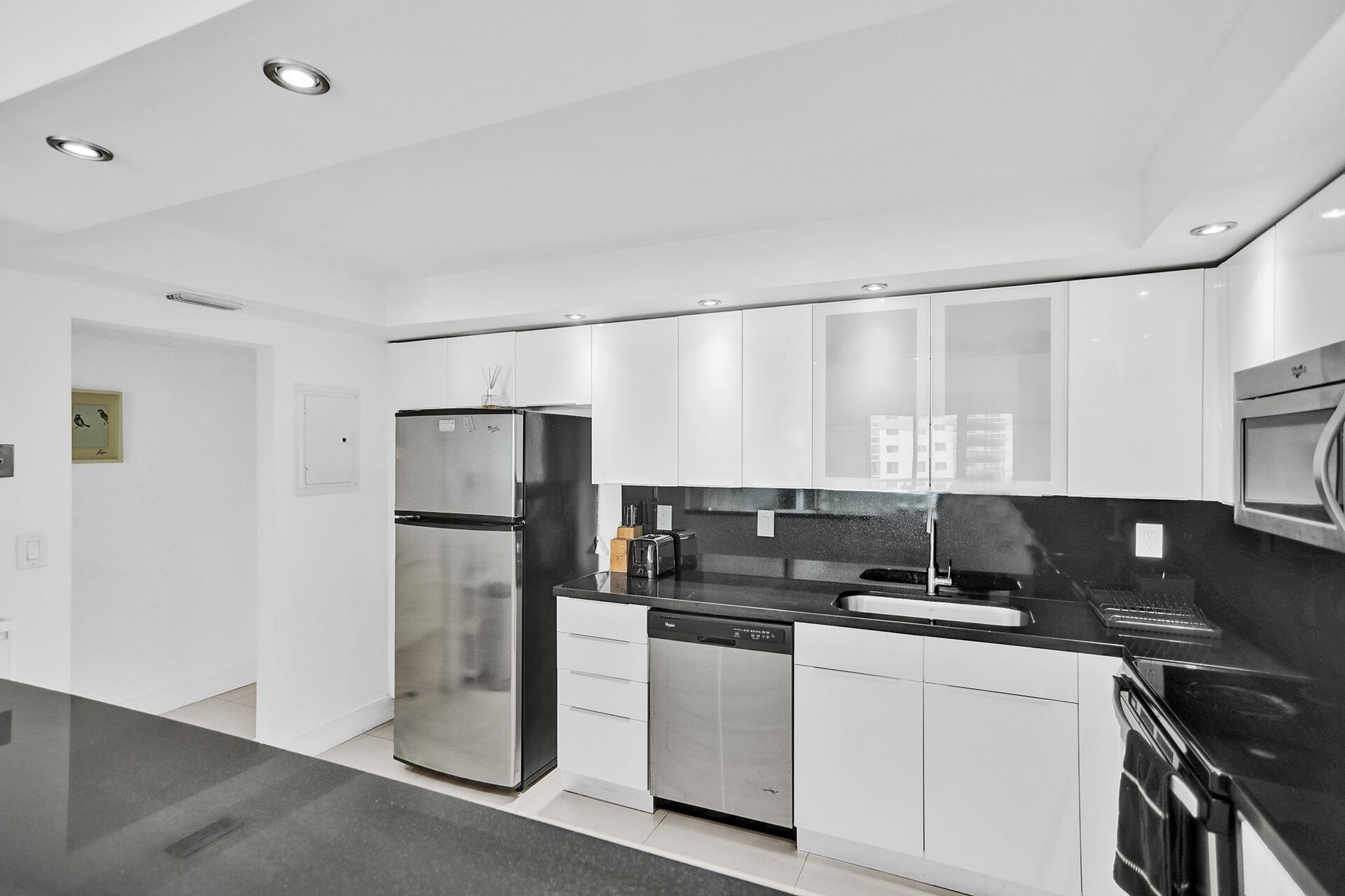 A modern kitchen with stainless steel appliances, white cabinetry, and a black countertop.