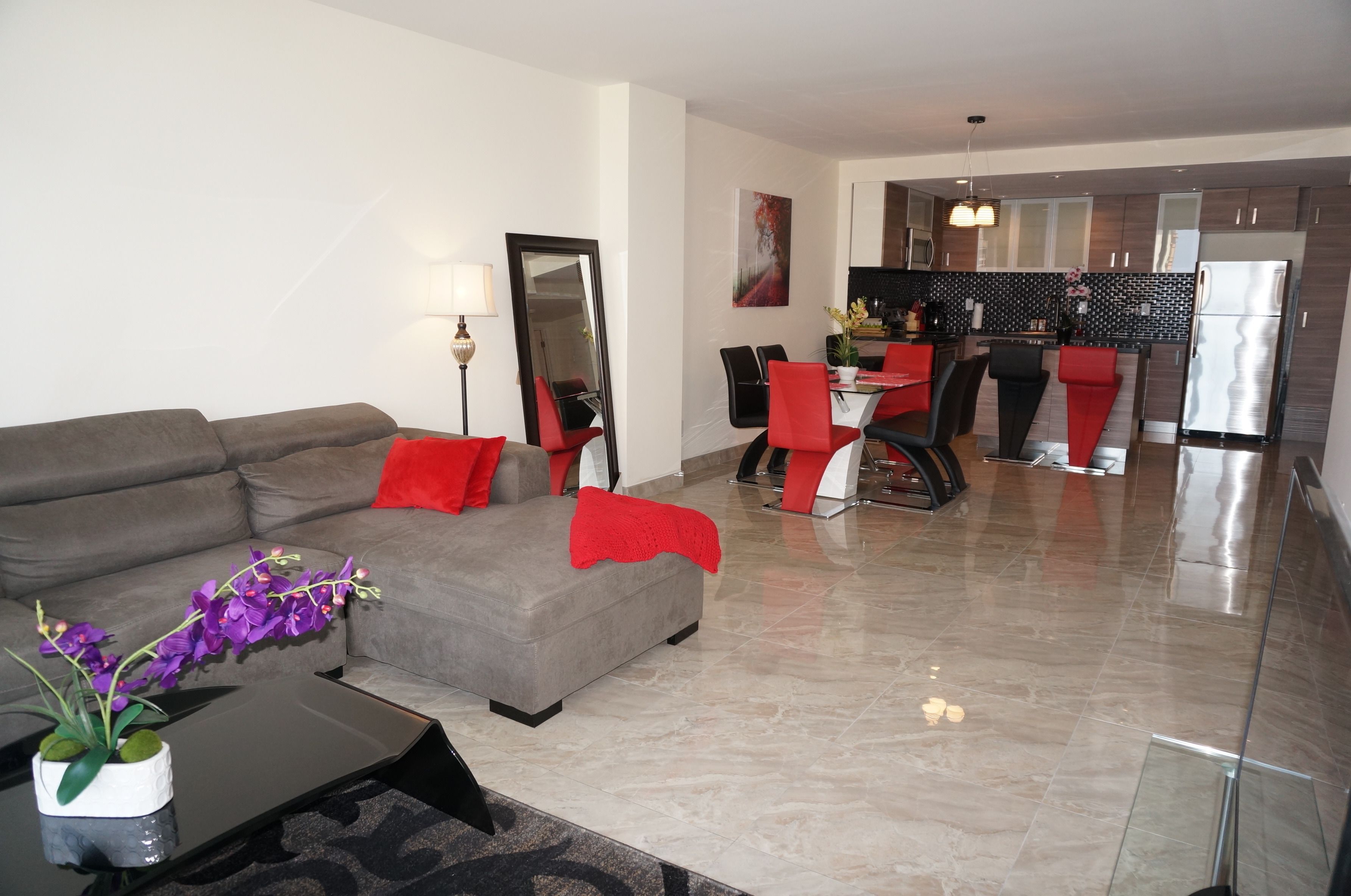 A modern living room with a grey sofa, red cushions, and a coffee table with a vase of purple flowers.