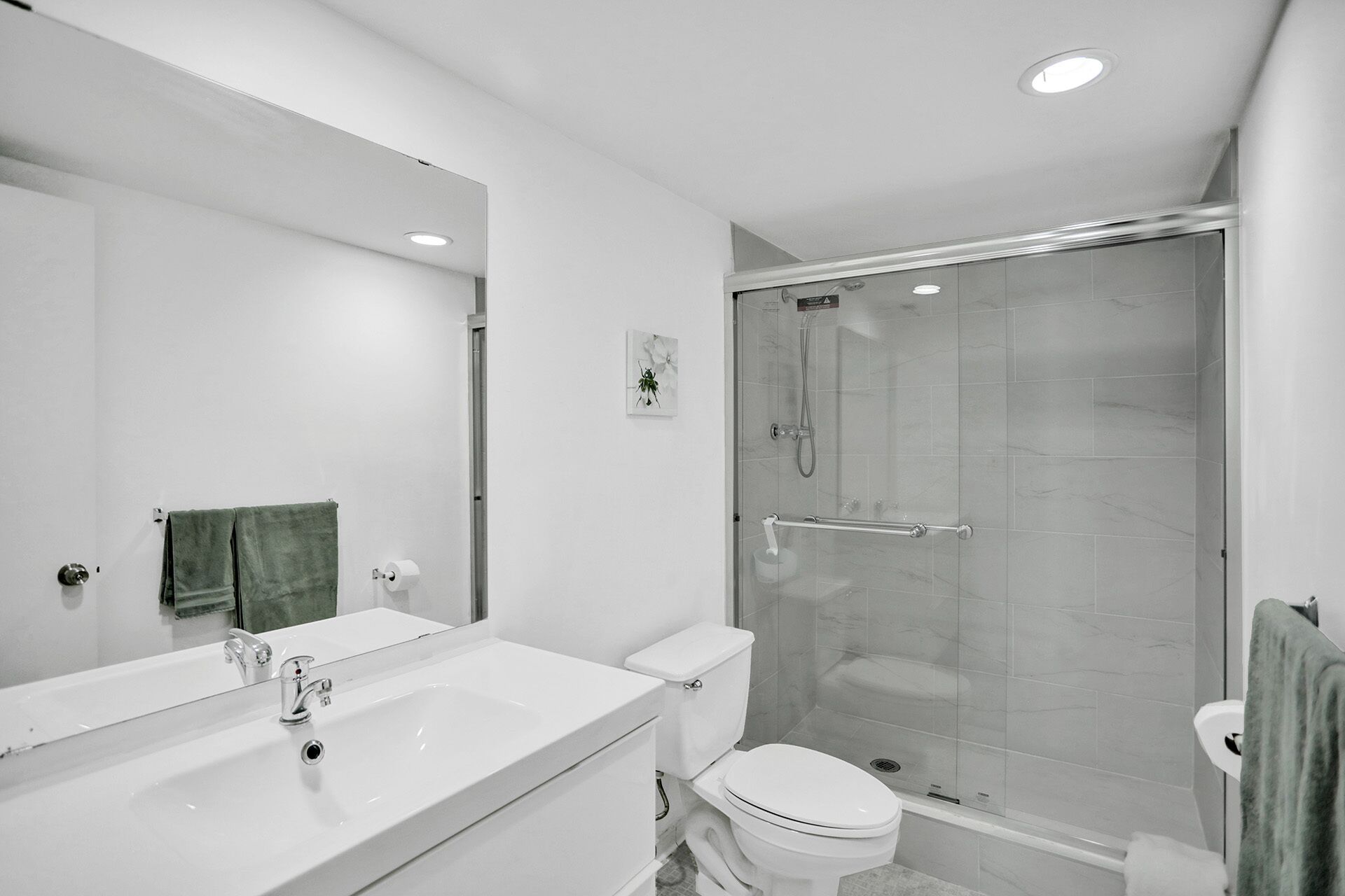 Une salle de bain moderne avec un grand miroir, un lavabo blanc, des toilettes et une douche à parois de verre.