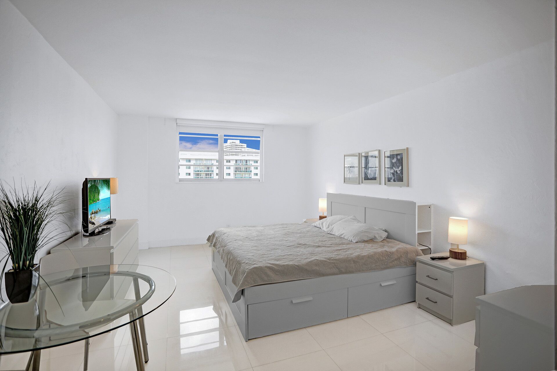 A modern bedroom with a bed, bedside tables, a glass table, and a TV.