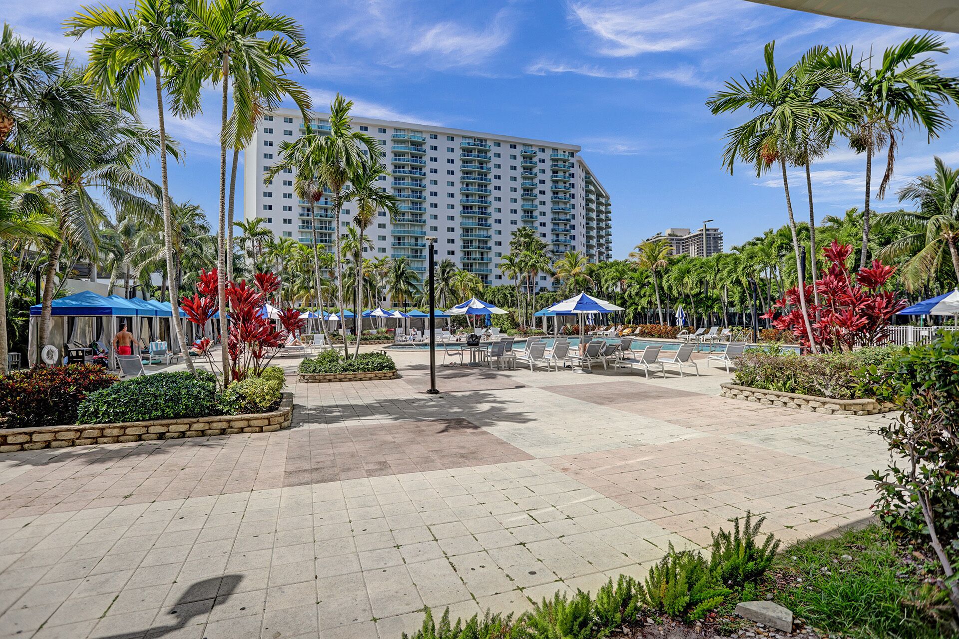 A resort pool area with palm trees, lounge chairs, and a large building in the background.
