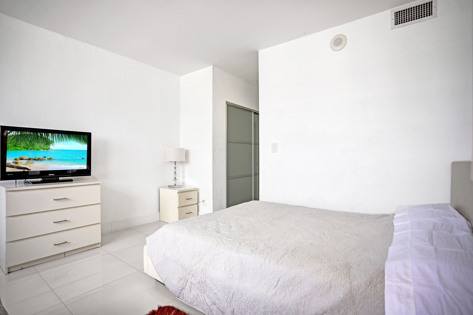 Una camera da letto con un letto, una TV su un comò, un comodino con una lampada e una porta che dà su un'altra stanza.
