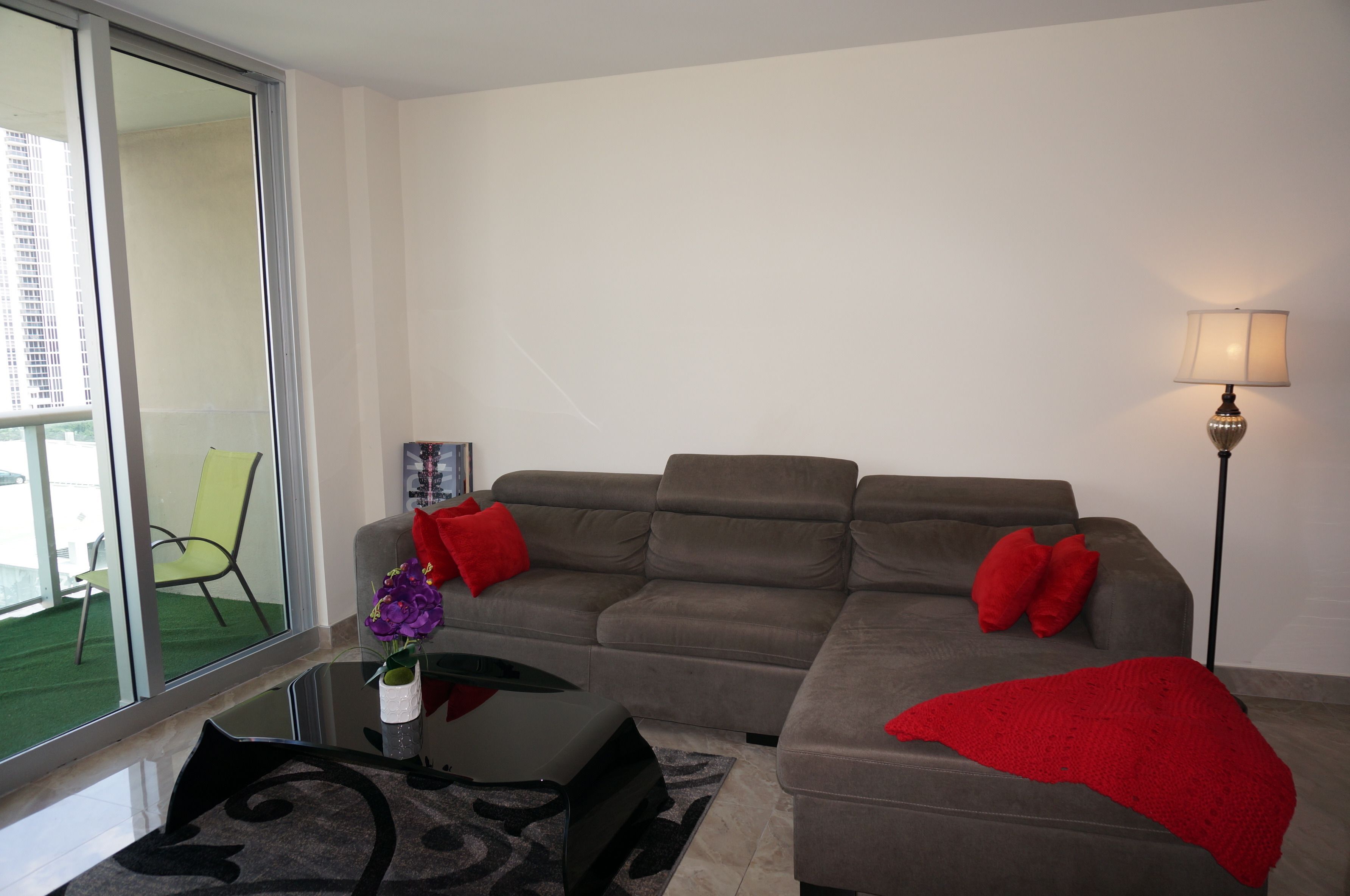 Een moderne woonkamer met een grijze bank, rode kussens, een glazen salontafel en een vloerlamp.