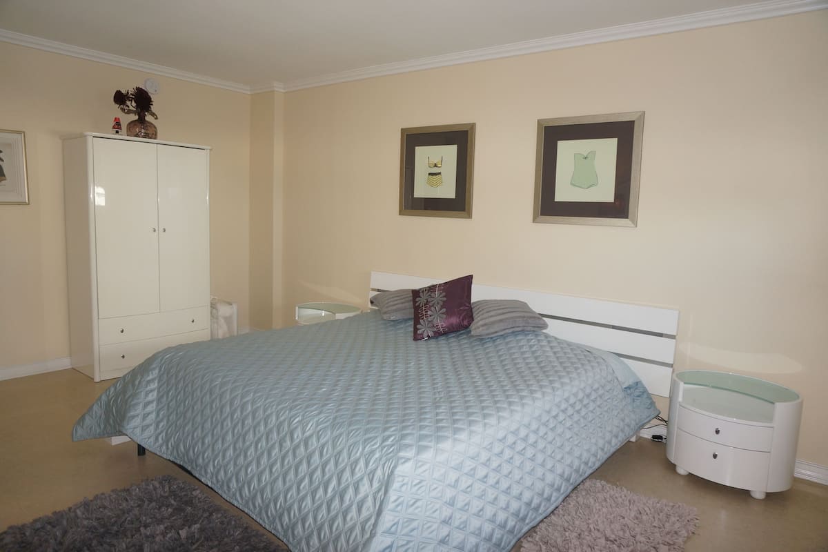 Une chambre à coucher comprenant un lit, une armoire, deux tables de chevet et des tableaux encadrés accrochés au mur.