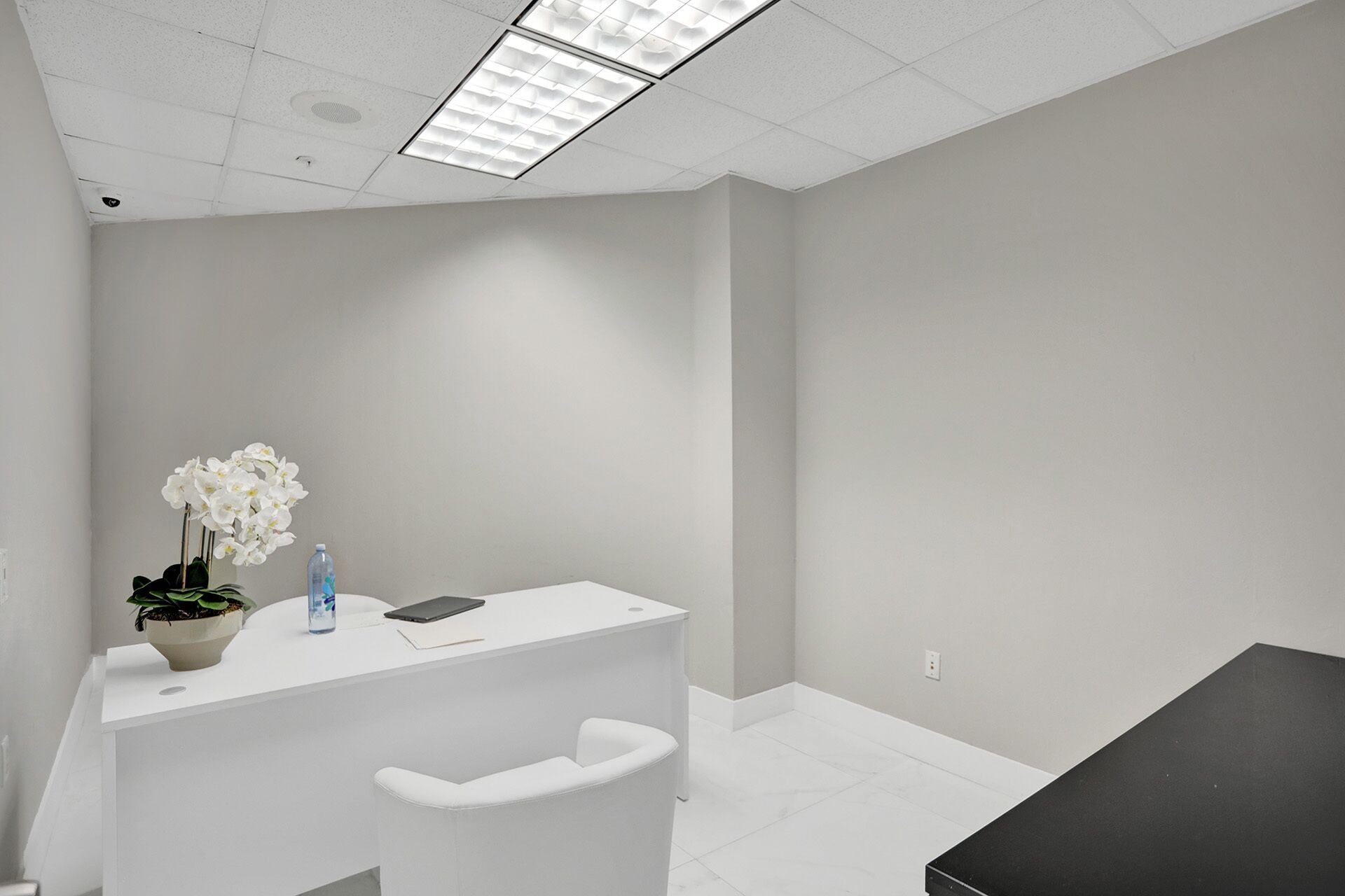 A clean, modern reception area with a white desk, a potted orchid, a water bottle, and a black tablet.