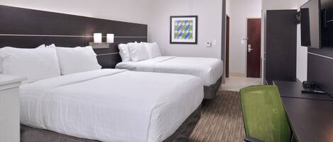 A hotel room with two beds, a desk, a chair, a ceiling fan, and a framed picture on the wall.
