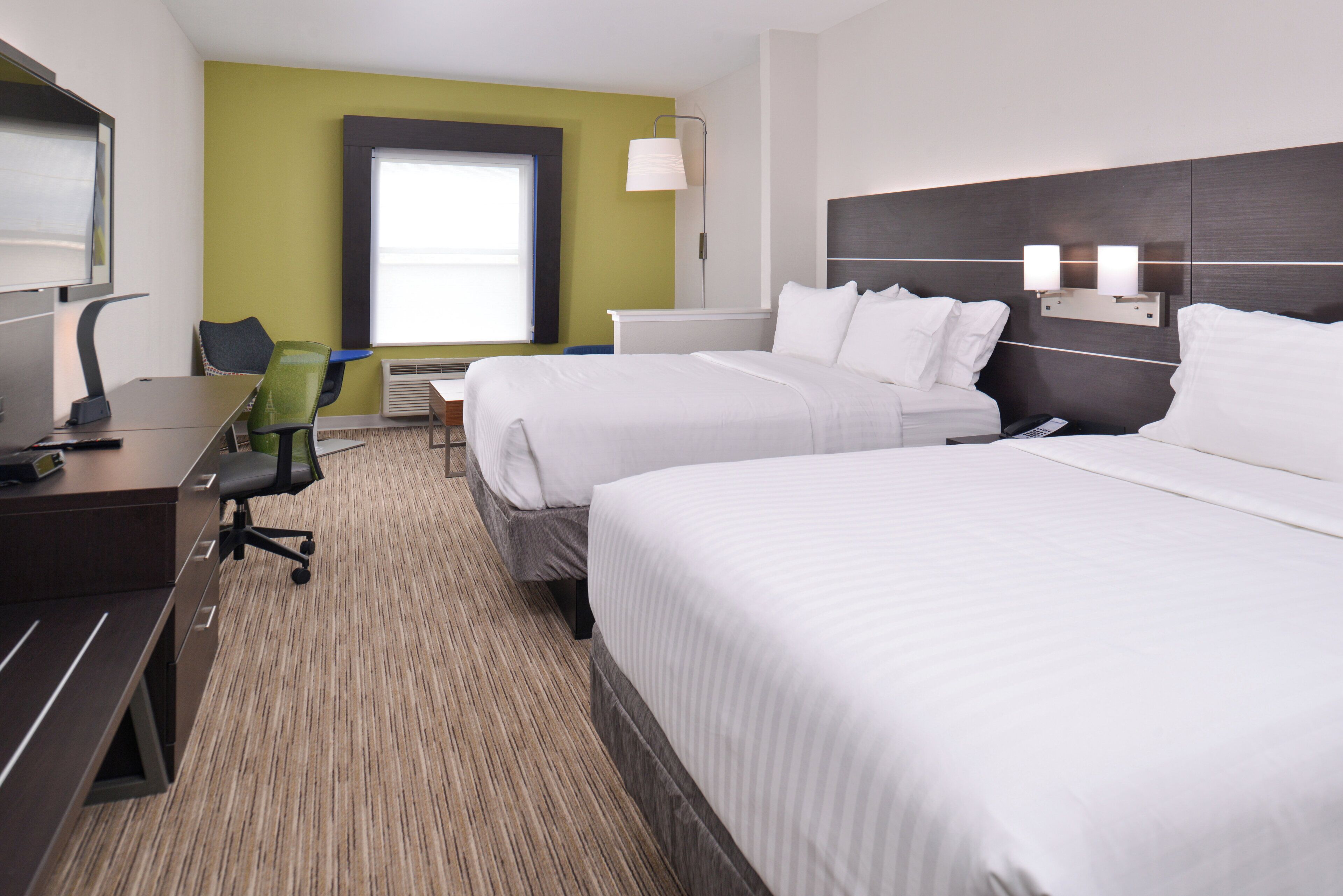 A hotel room with two beds, a desk, a chair, a TV, and a window.