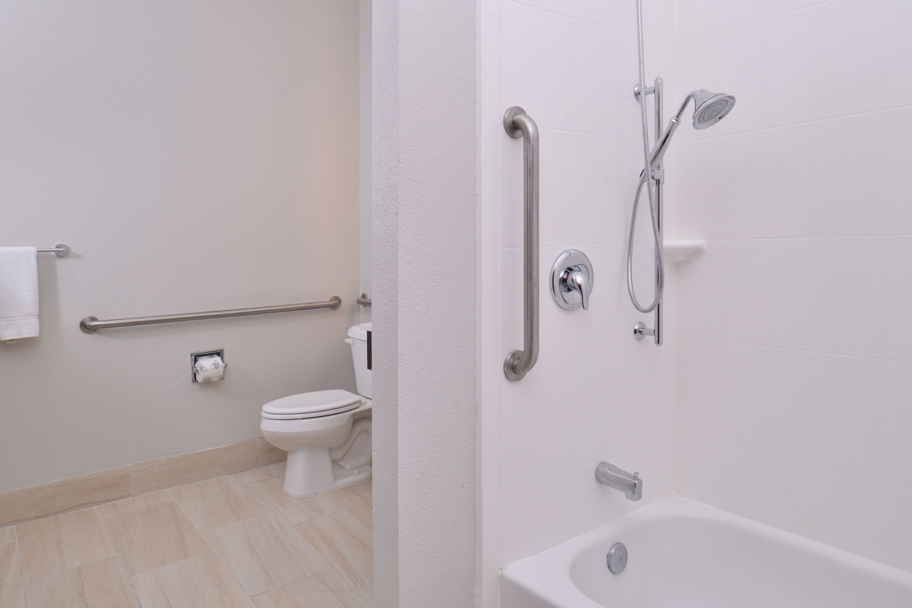 Un baño con inodoro, barra de apoyo, ducha con cabezal de ducha manual y bañera.
