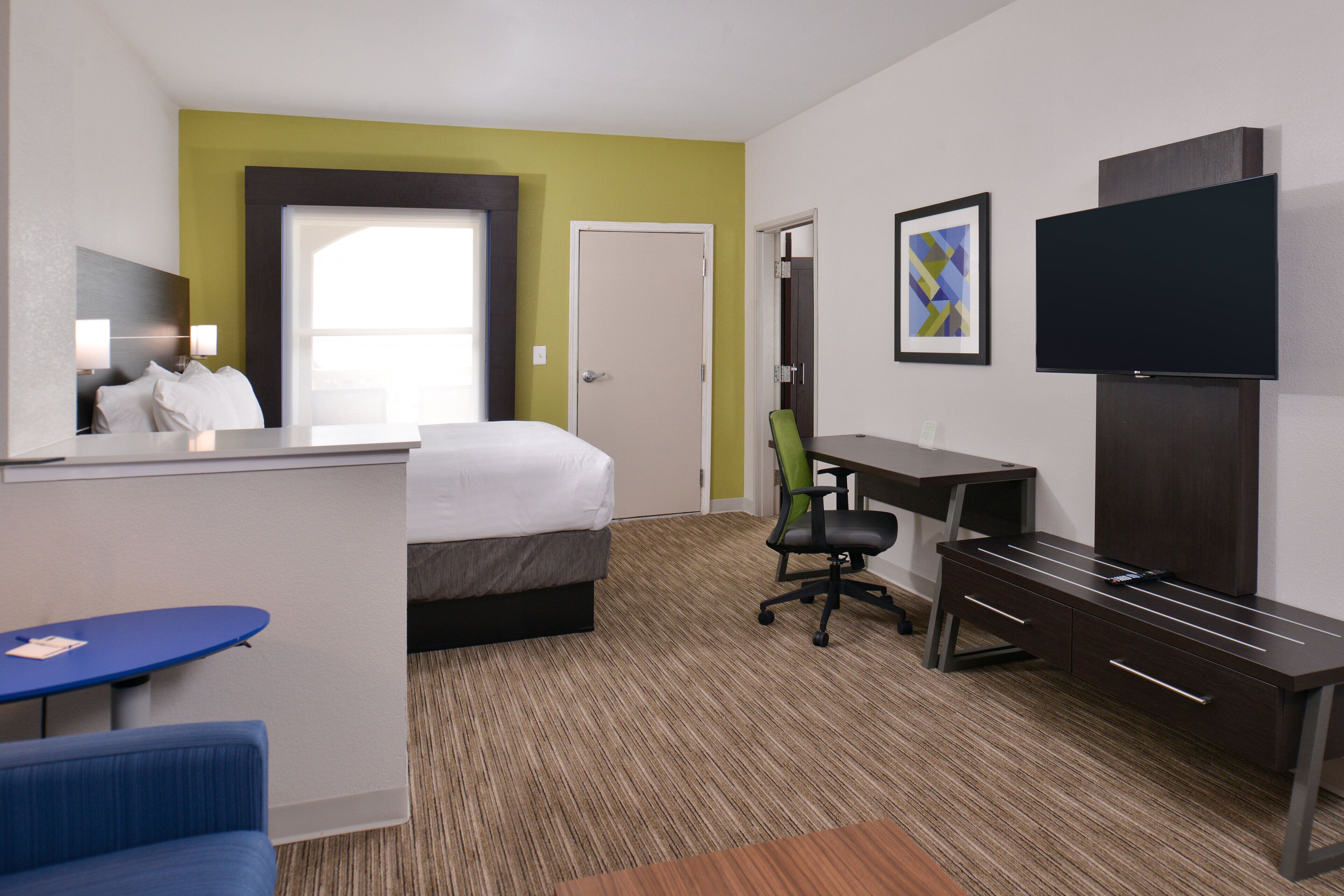 A hotel room with a bed, desk, chair, TV, and a small table.