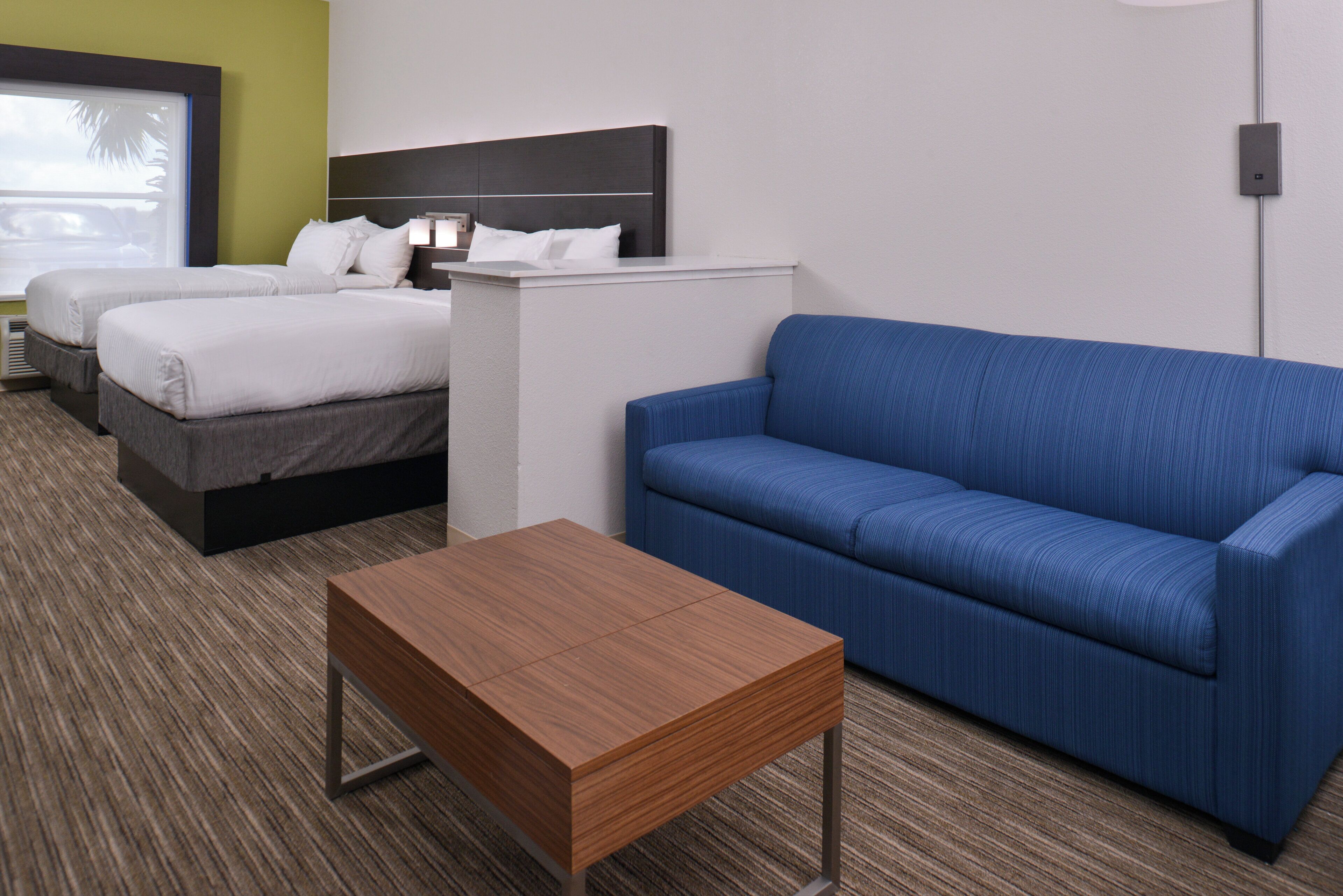 Una habitación de hotel con dos camas, un sofá azul y una mesita de madera.