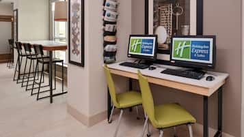 A hotel workspace with two monitors, a desk, and chairs.