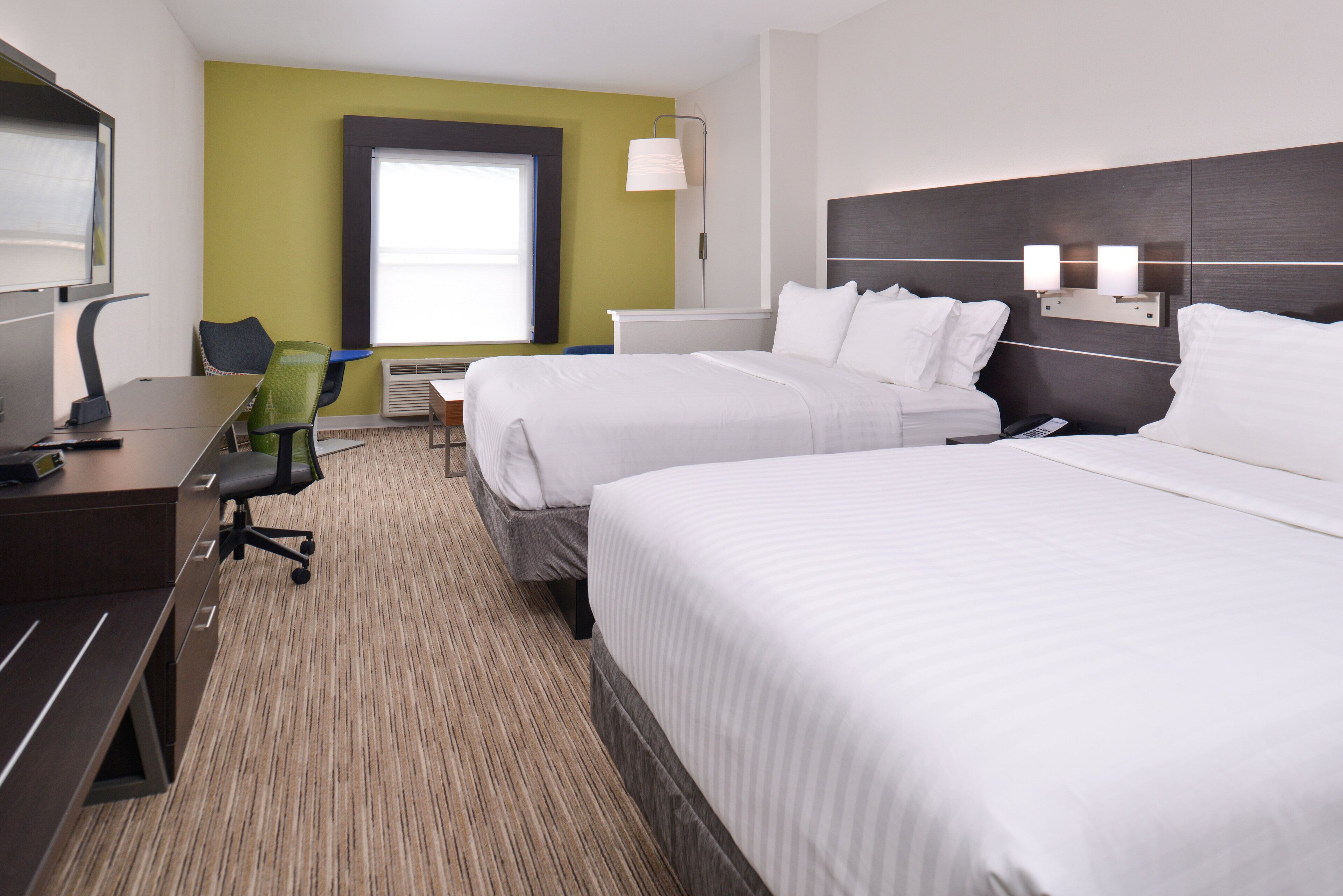 Een hotelkamer met twee bedden, een bureau, een stoel, een televisie en een raam.