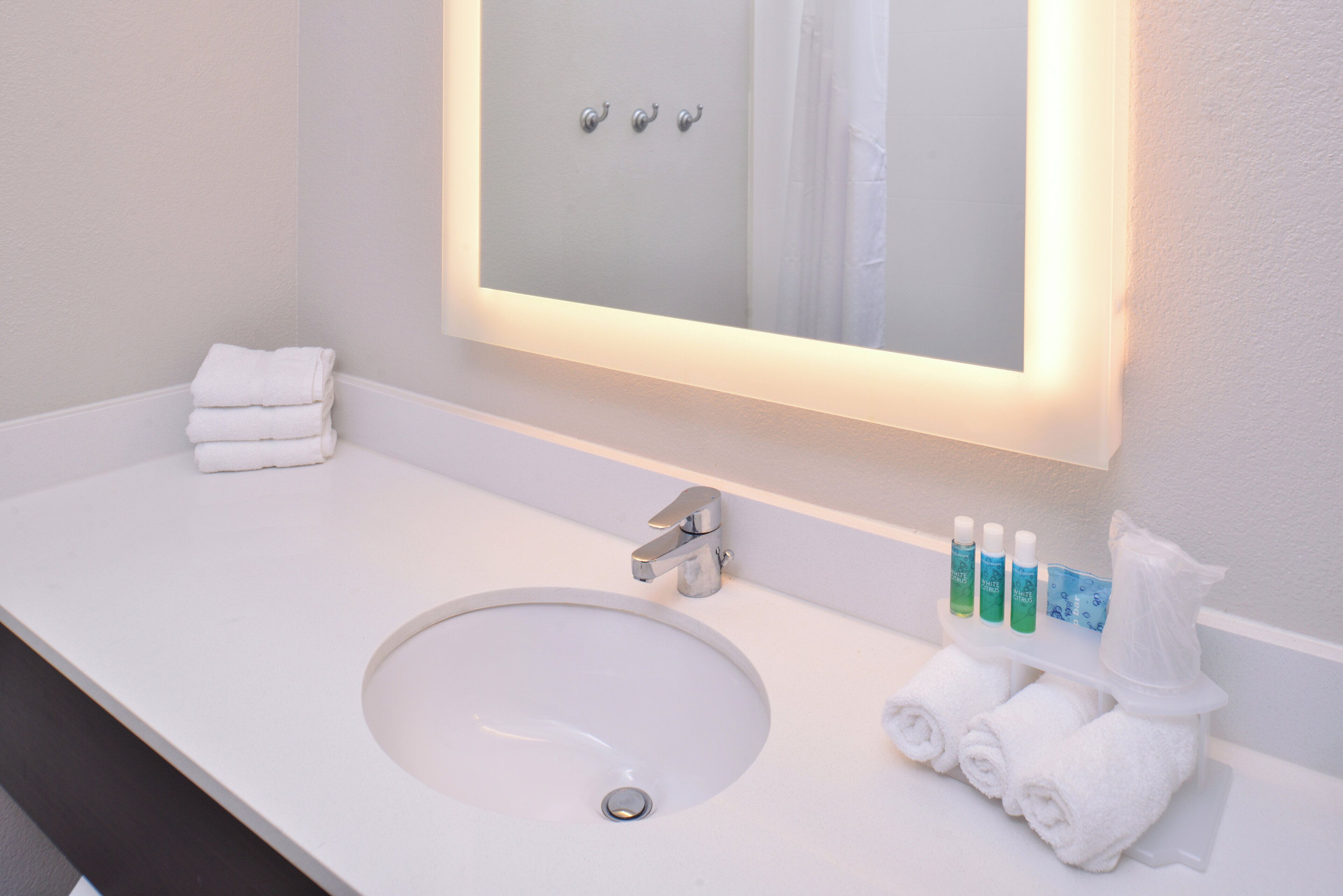 A hotel bathroom with a white sink, a mirror, and toiletries.